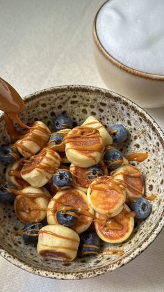 a bowl filled with banana slices and blueberries next to a cup of coffee on a table