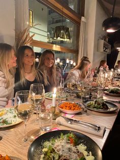 three women sitting at a table with plates of food and glasses of wine in front of them