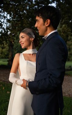 a man and woman standing next to each other in front of some trees at sunset