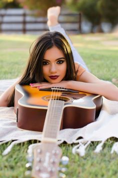 a woman laying on top of a blanket holding an acoustic guitar in her hand and looking at the camera