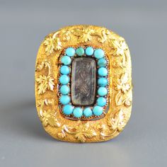 A beautiful antique early Victorian period (1837-1901) turquoise keepsake brooch conversion ring in 15k/14k  yellow gold. This antique ring began life as an early Victorian brooch that my bench jeweler expertly converted into a wearable ring for today. It features a central locket compartment with a beveled crystal cover that contains a beautiful plait of brown hair surrounded by a halo of natural turquoise that have aged beautifully to varying hues in cut down collet settings all surrounded by a wide gold textured band with an applied wreath of ivy leaves. The back has a smooth panel and a new complimentary split shank has been added. The original brooch tests for 15k gold and the new band is 14k gold. Ring size: US 7.5 and sizable Ring face measures approximately: 25mm high x 20mm wide W Vintage Yellow Gold Turquoise Cabochon Ring, Antique Yellow Gold Turquoise Cabochon Ring, Vintage Yellow Gold Turquoise Ring Hallmarked, Antique Yellow Gold Turquoise Ring For Anniversary, Heirloom Gold Turquoise Gemstone Ring, Heirloom Hallmarked Yellow Gold Turquoise Ring, Vintage Yellow Gold Turquoise Wedding Ring, Heirloom Yellow Gold Turquoise Cabochon Ring, Vintage Yellow Gold Turquoise Ring For Wedding