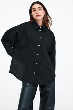 Our Ezra Shirt is a capsule wardrobe dream for your closet. Crafted from 100% crisp European poplin cotton, she offers a classic button-up silhouette in front, but with a cropped back for modern edge. Say hello, as well, to her diagonal seams at the front, sleek collar and long dolman sleeves finished with mother-of-pearl button cuffs. Wear Ezra tucked, tied or open and free—she never fails to inspire new looks.[SPLIT] Rocio, in black and in light blue, is 5'9.5" (175 cm) tall, wearing size XS. Fall Poplin Shirt, Chic Poplin Shirt For Work, Chic Cotton Shirt With Shirttail Hem, Chic Collared Poplin Top, Daywear Poplin Tops With Button Closure, Daywear Tops With Button Closure, Poplin Tops With Button Closure For Daywear, Chic Button-up Poplin Blouse, Relaxed Fit Poplin Tops With Button Cuffs