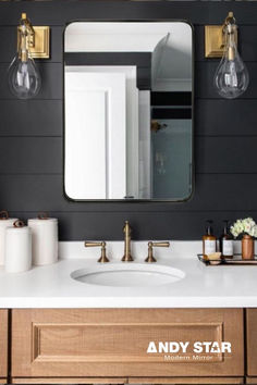 a bathroom with black walls and white counter tops, gold fixtures and lights on the wall