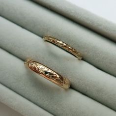 two gold wedding rings sitting on top of white velvet