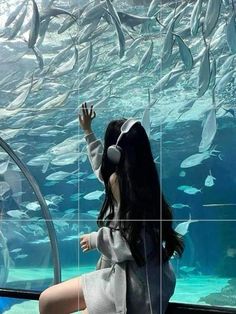 a woman is looking at fish in an aquarium with her hand up to the water