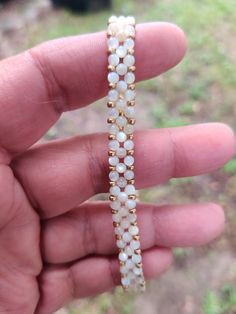 a hand holding a gold and white beaded bracelet