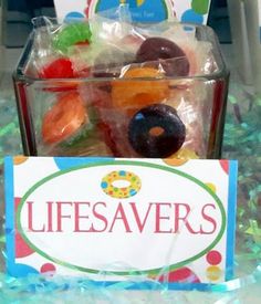 a glass container filled with gummy bears on top of a table next to a sign that says lifesavers