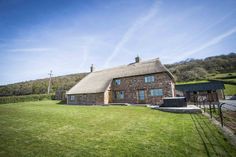 a stone house with a thatched roof in the middle of a grassy field next to a hill