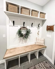 a white bench sitting under a window next to a shelf filled with baskets and wreaths