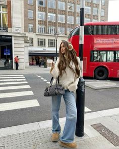 a woman standing next to a pole with a cup of coffee in her hand and a red double decker bus behind her