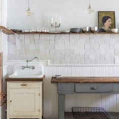 an old kitchen with a sink, counter and shelves on the wall above it that have pictures hanging over them