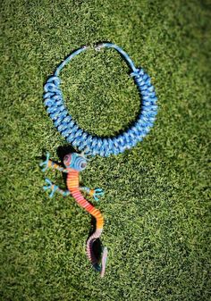 a blue and orange lizard necklace laying on top of a green grass covered field next to a string