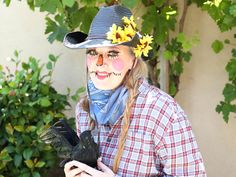 a woman with painted face and nose holding a black bird in front of some bushes