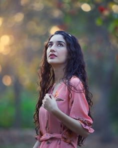 a woman in a pink dress looking up into the sky with her hands folded on her chest