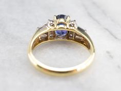 "We love the modernist style of this stunning engagement ring. The flat, smooth sides are interesting, and the top of the shoulders have a beautiful curve, set with bold baguette and round cut diamonds. The center stone is a pretty, excellent shade of violet-hued blue. This color is the benchmark for fine Sapphire, and indicative of Sri Lanka, where we purchased the stone! Metal: 18K Yellow Gold Gem: Sapphire 1.58 Carats Gem Measurements: 7.4 x 6.0 mm, Oval Accents: 12 Diamonds totaling .36 Cara Shades Of Violet, Gold Sapphire Ring, Ring Sapphire, Sapphire And Diamond Ring, Stunning Engagement Ring, Sapphire Engagement Ring, Sapphire Jewelry, Anniversary Bands, Sapphire Engagement