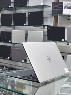 an open laptop computer sitting on top of a glass table in a room filled with shelves