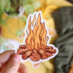 a hand holding up a sticker with a campfire on it