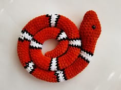 an orange and white knitted snake on a white surface