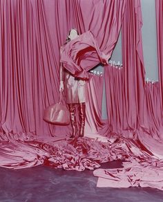 a woman standing in front of a pink curtain holding a purse and looking at it