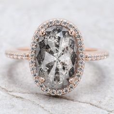 an oval cut diamond surrounded by small diamonds in a rose gold halo setting on top of a white marble surface