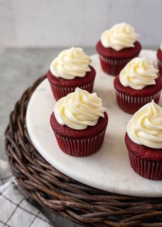 several red velvet cupcakes with white frosting on a wicker platter