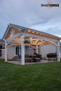 a covered patio with lights on it and a grill in the back yard next to some grass