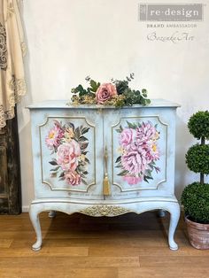 an old dresser with flowers painted on the doors and drawers is sitting next to a potted plant