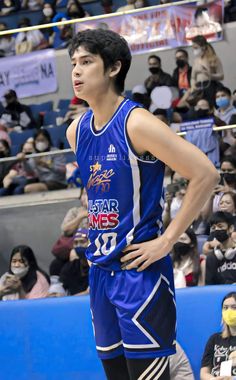 a young man standing on top of a basketball court wearing a blue uniform and holding his hands on his hips