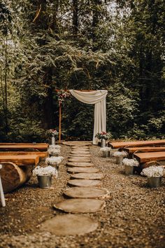 an outdoor ceremony setup with wooden benches and flowers on the aisle, surrounded by greenery