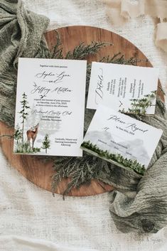 the wedding stationery is laid out on a wooden platter with pine trees and evergreens