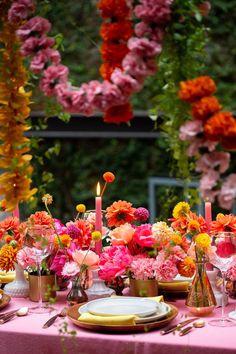 the table is set with pink and orange flowers, candles, plates and napkins