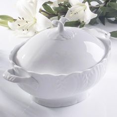 a white bowl sitting on top of a table with flowers in the backgroud