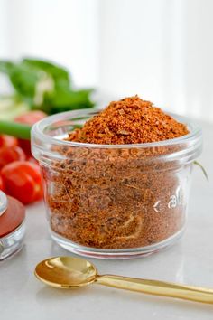 a glass bowl filled with spices next to some tomatoes and other vegetables on a table