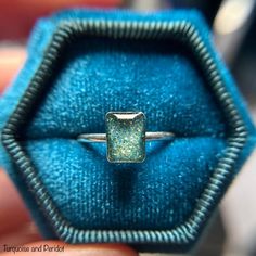 a close up of a person holding a ring in a blue velvet box with a diamond on it