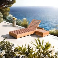 a wooden chaise lounge sitting on top of a patio next to the ocean