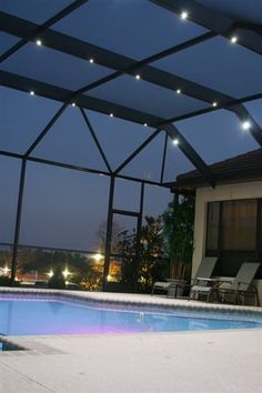 an empty swimming pool in front of a house at night with lights on the roof