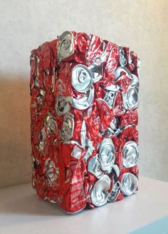 a box made out of soda cans sitting on top of a table next to a wall