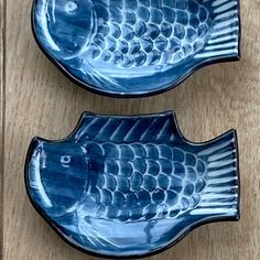 two blue fish shaped dishes sitting on top of a wooden table next to each other