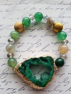 Give your wrist a bold, natural shine with the addition of beautiful crystals! Eclectic in style, this beautiful open green dyed agate pendant offers an irregular shaped druzy cluster with metallic edges of gold foil. The pendant is a great  focal on this bracelet. The druzy is 1.5 inches (1.25 inches in width). The green druzy ia accompanied by green and brown agate rounds, along with facet crystal rondelles. The agate rounds and crystal mixture has swirling patterns and shining facets. The bra Green Stretch Bracelet With Natural Stones, Elegant Green Stretch Bracelet With Natural Stones, Green Gemstone Stretch Bracelet Gift, Green Round Crystal Bracelet For Spiritual Use, Green Agate Jewelry With Natural Stones, Green Agate Round Crystal Bracelet, Green Crystal Bracelet For Spiritual Healing, Green Bohemian Beaded Bracelets With Stones, Elegant Green Agate Crystal Bracelet