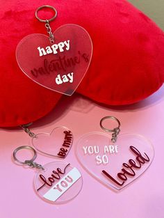 two heart shaped key chains sitting next to a red pillow with the words happy valentine's day on it