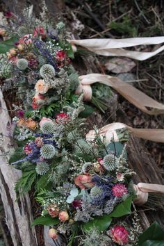 an arrangement of flowers and greenery is lined up on a wooden bench in the woods