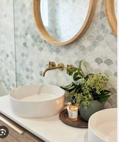 a white sink sitting under a bathroom mirror next to a wooden bowl filled with flowers