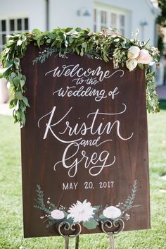 a wooden sign with flowers and greenery on it that says welcome to the wedding of kirstin and greg