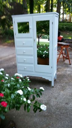 a small white cabinet sitting in the middle of a yard with flowers growing out of it