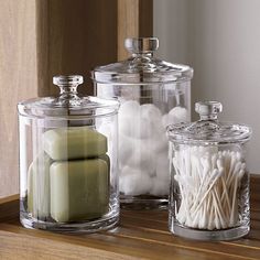 three glass containers filled with candles on top of a wooden table