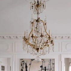 a chandelier hanging from the ceiling in a white room with paintings on the walls