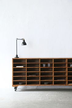 a large wooden shelf with cups on it and a lamp next to it in front of a white wall