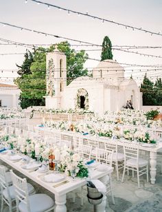 an outdoor wedding setup with white flowers and greenery on the tables, surrounded by string lights