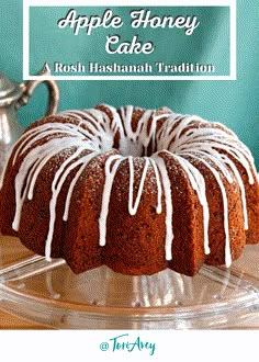 an apple honey cake with white icing on a glass platter next to a teapot