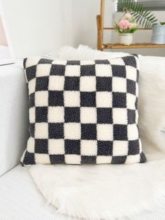 a black and white checkered pillow sitting on top of a couch next to a plant